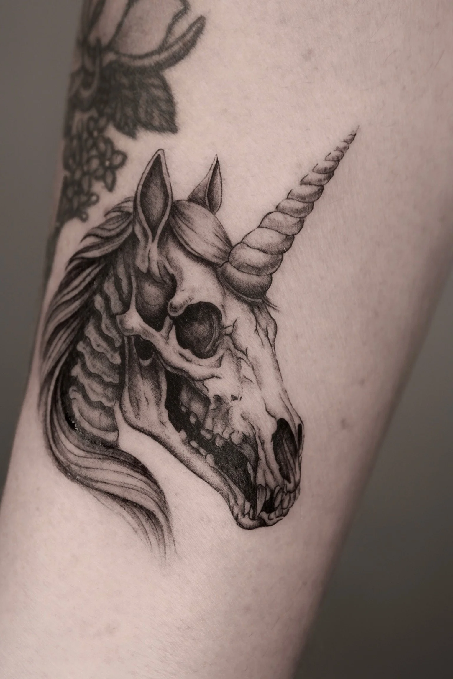 Tattoo of a unicorn skull with a spiral horn and detailed mane.