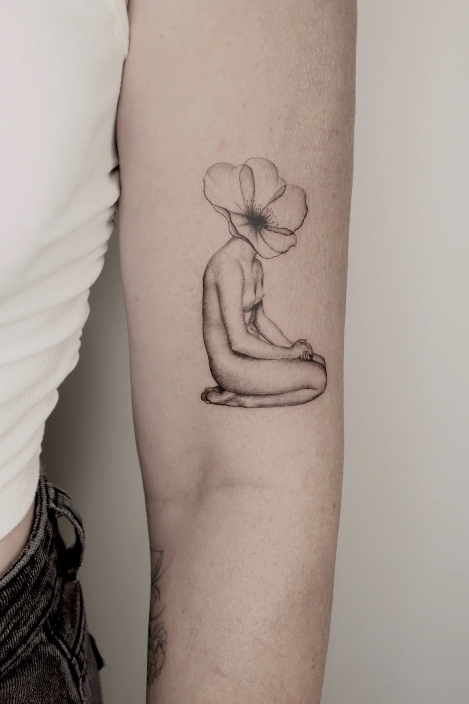 Tattoo of a kneeling woman with a large flower as her head on a person's upper arm.