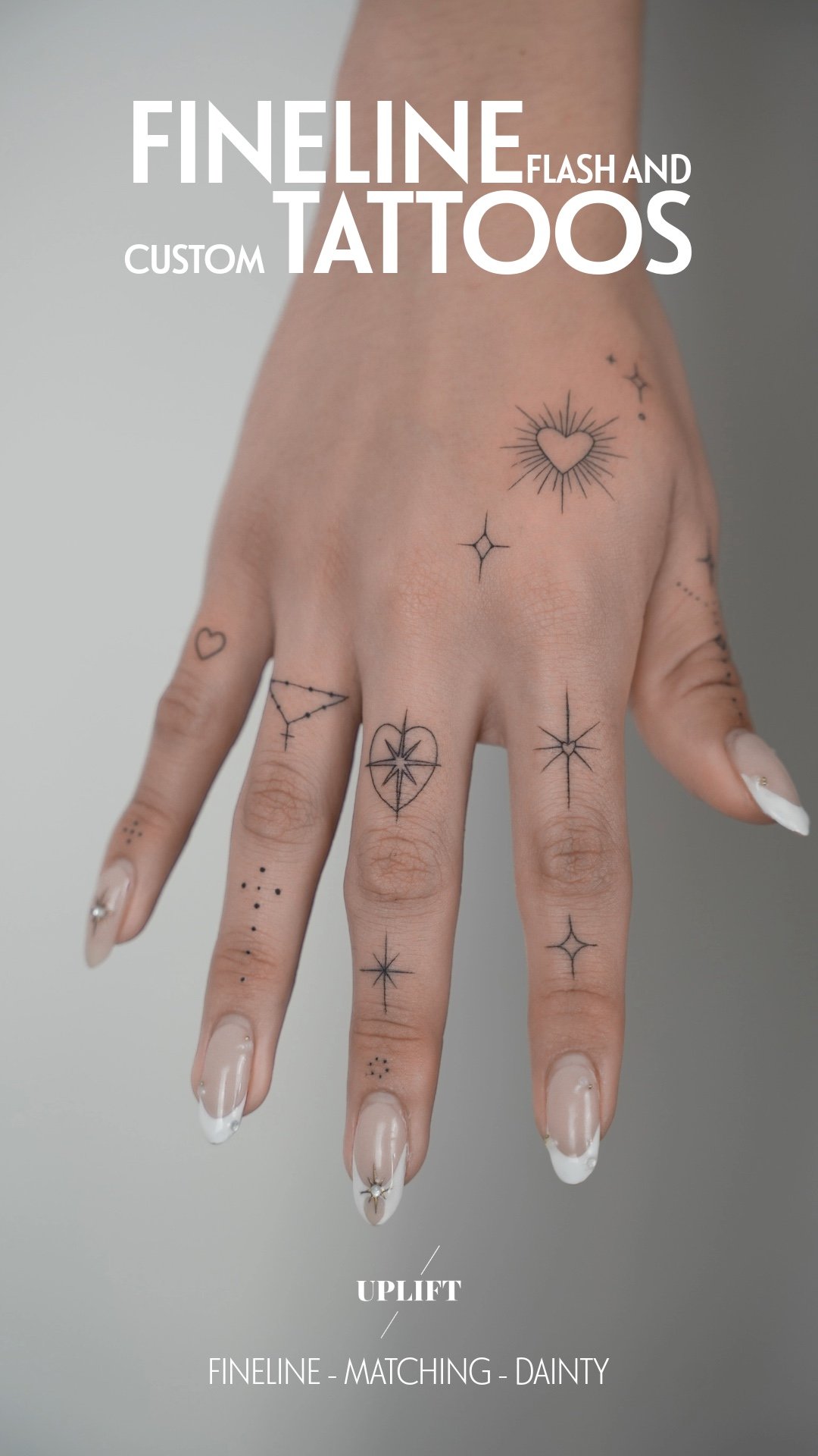 Close-up of a hand with multiple small black line tattoos, including hearts, stars, and geometric designs, on fingers and hand.