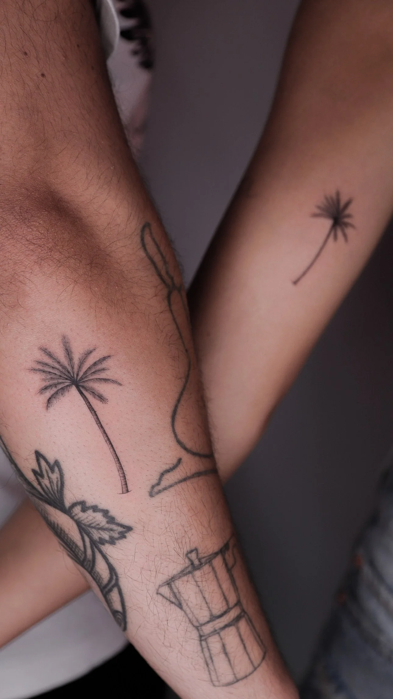 Close-up of a person’s arm and side with several minimalistic tattoos, including two dandelions, a bottle, and some abstract line art.