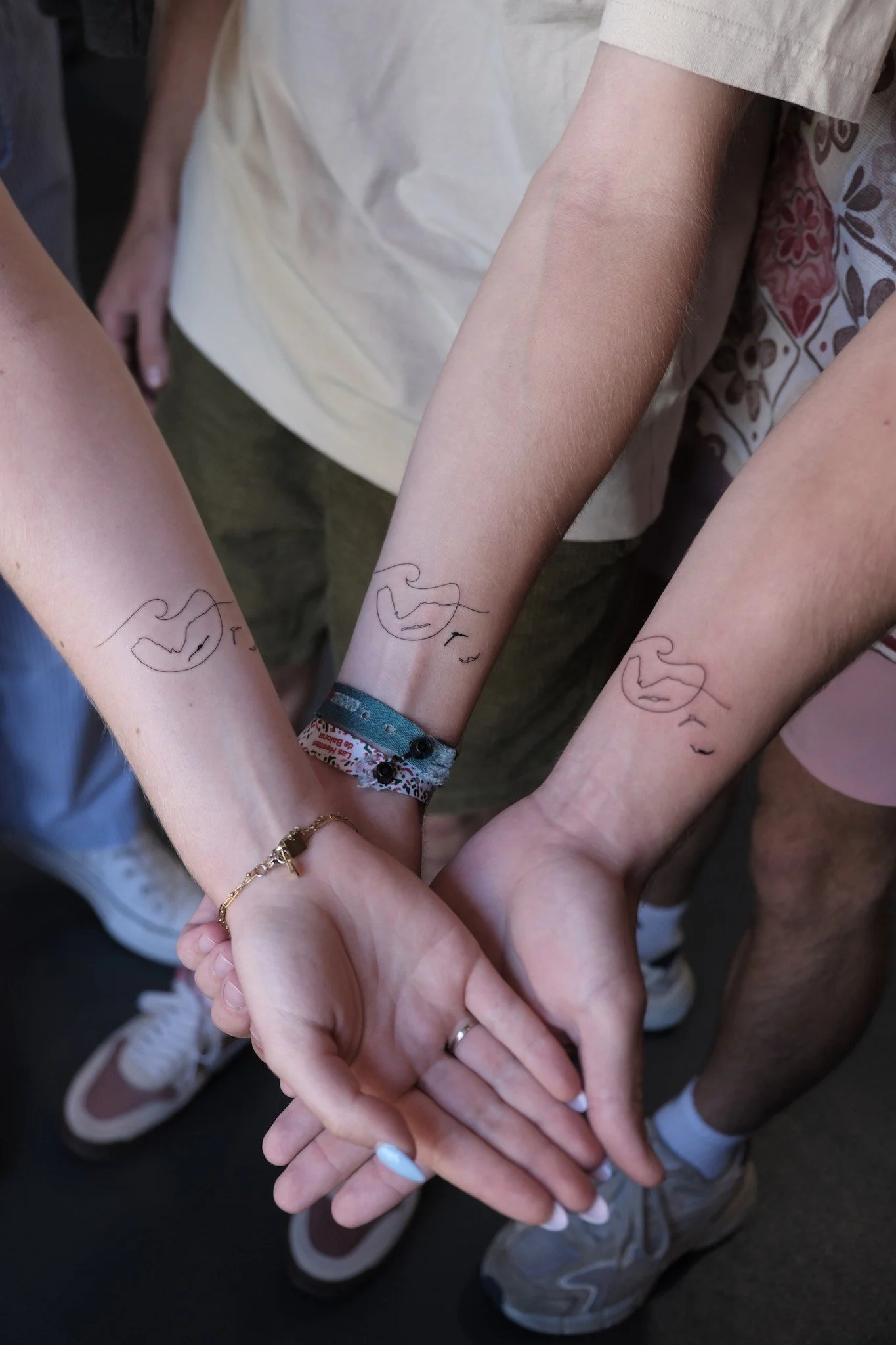 Group of people with their hands stacked together, wearing matching temporary tattoos of a face outline and various jewelry, in a show of unity.