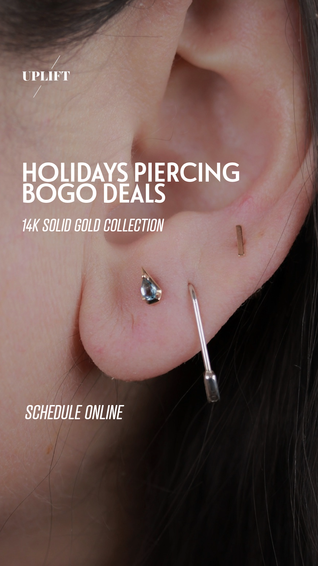 Close-up of a person's ear with multiple piercings, including a black gemstone stud, a thin gold bar, and a clear medical piercing needle.