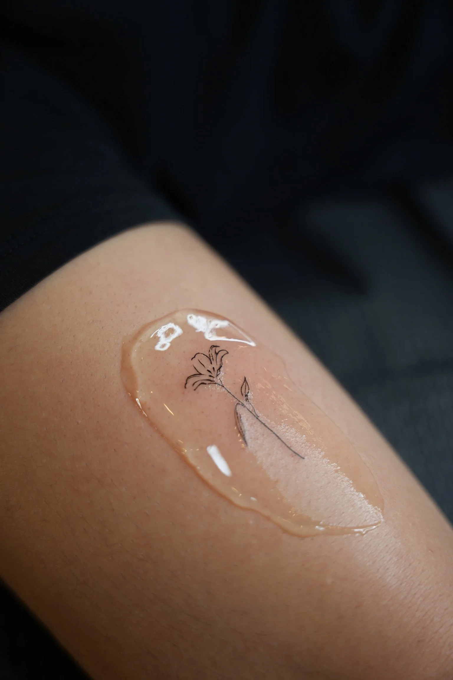A person's arm with a clear gel patch containing a small, simple line drawing of a flower.