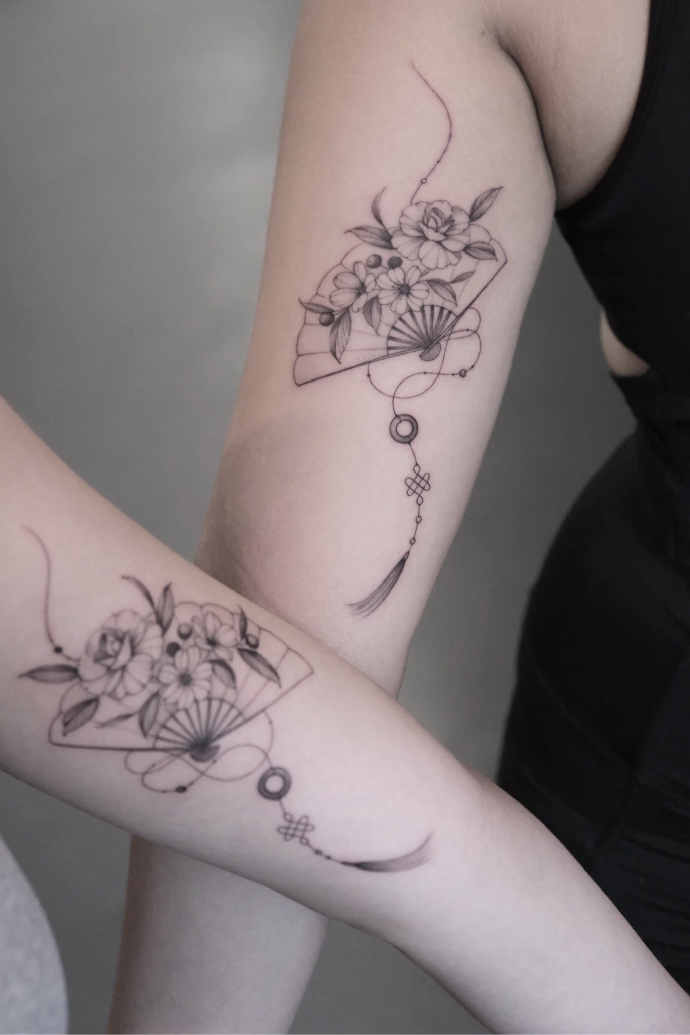 Black and gray tattoo of flowers and a traditional paper fan on a person's upper arm.