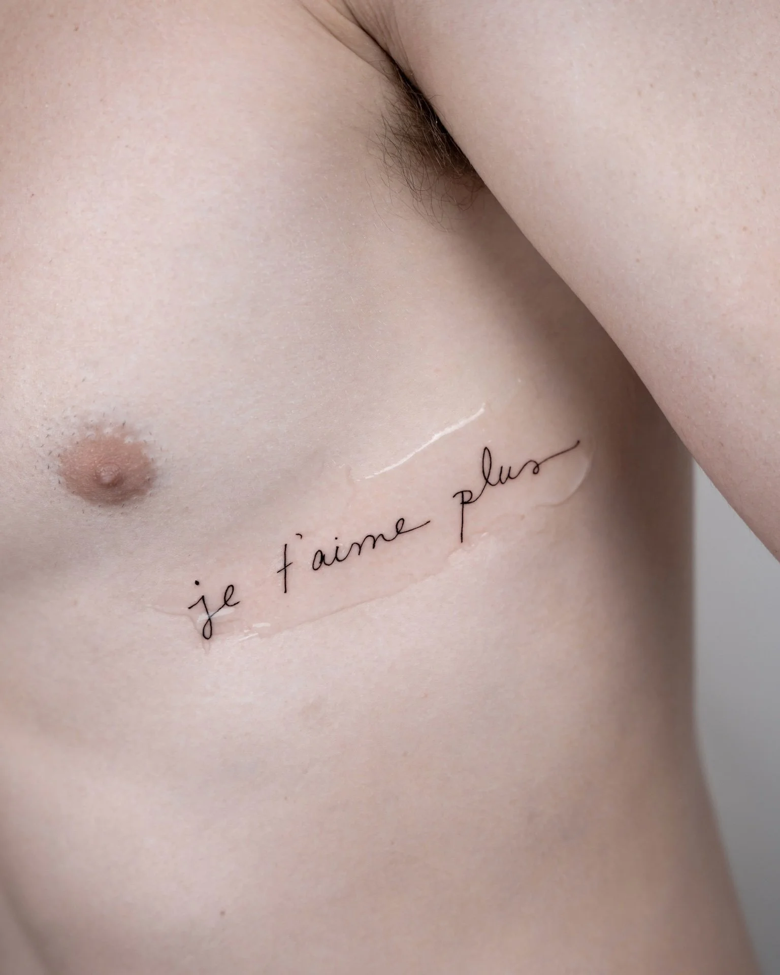 Close-up of a woman's side torso with French text tattooed under her breast reading 'Je t'aime plus'.