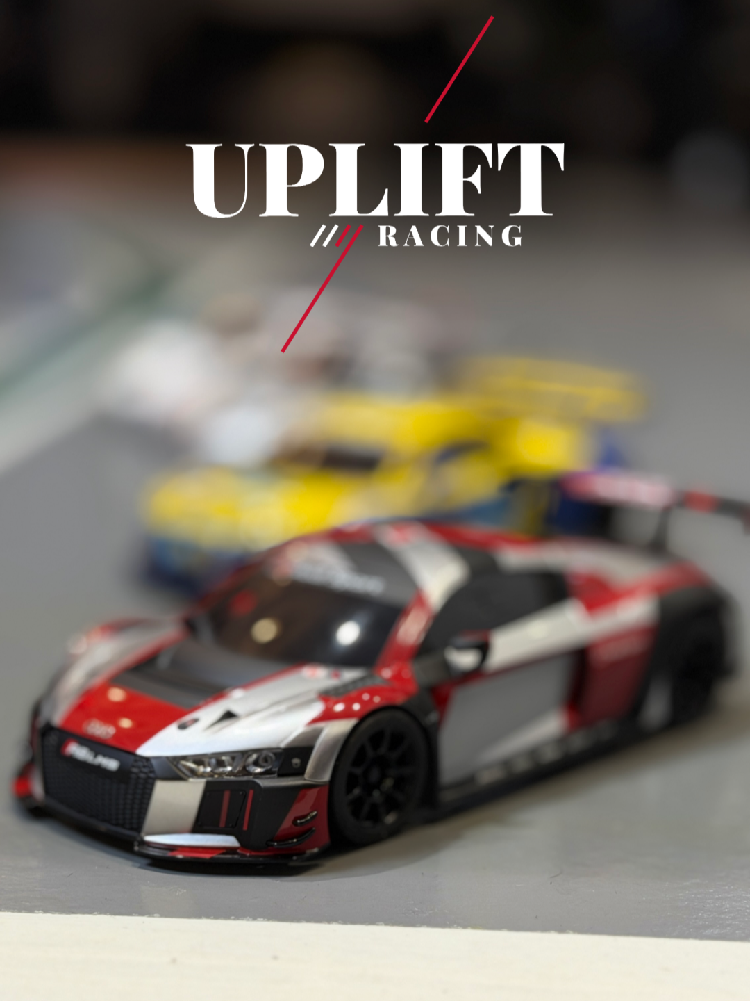 A model race car with a red, white, and black paint job in focus, with blurred background of other similarly styled cars.