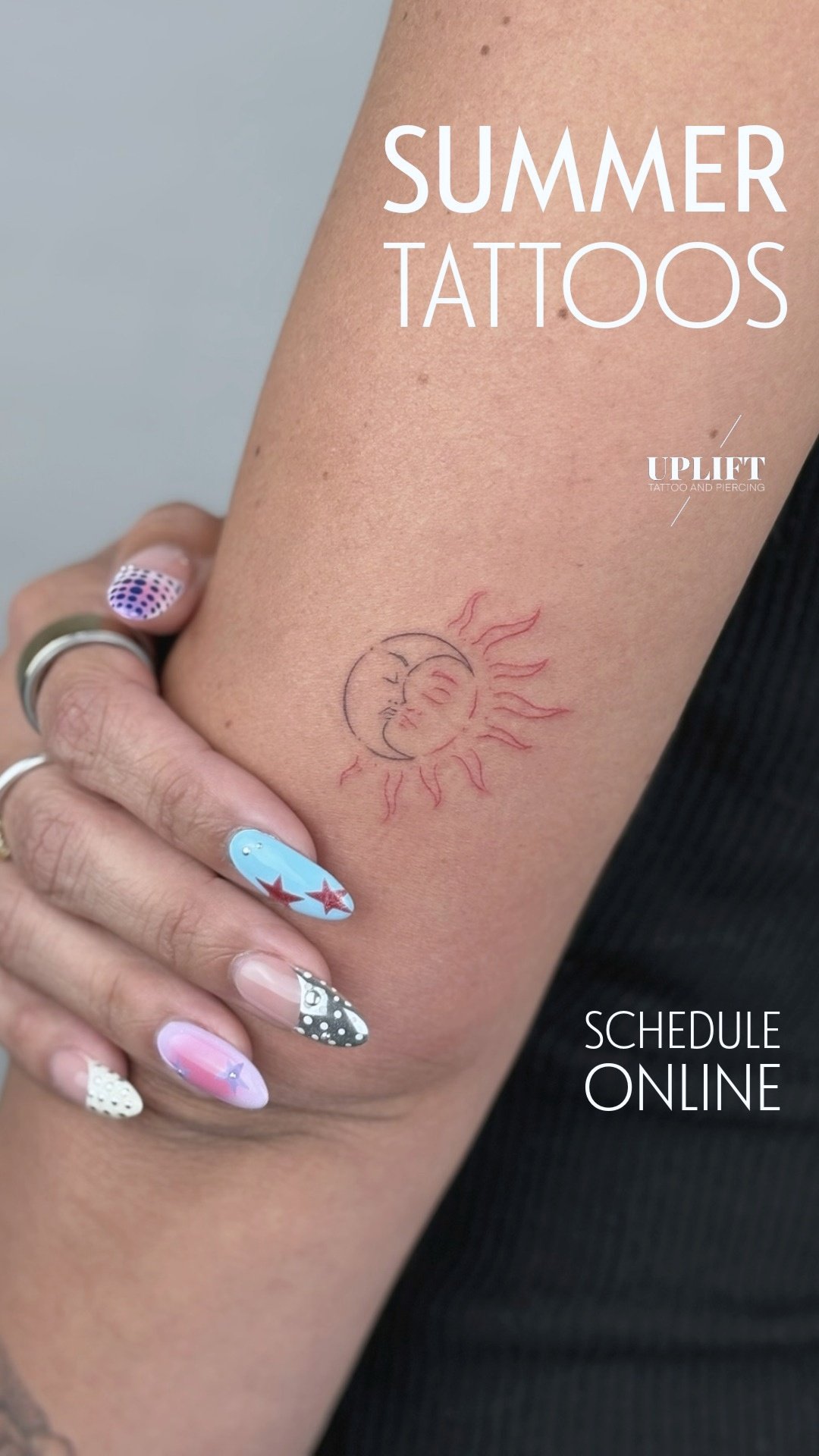 A person's arm with a small sun and moon tattoo, and colorful nail art on their fingers.