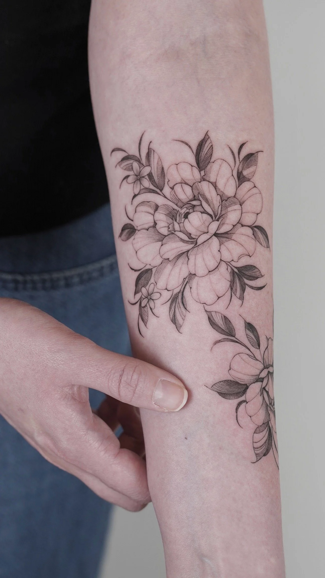 Black and gray floral tattoo featuring large flowers and leaves on a person's forearm.