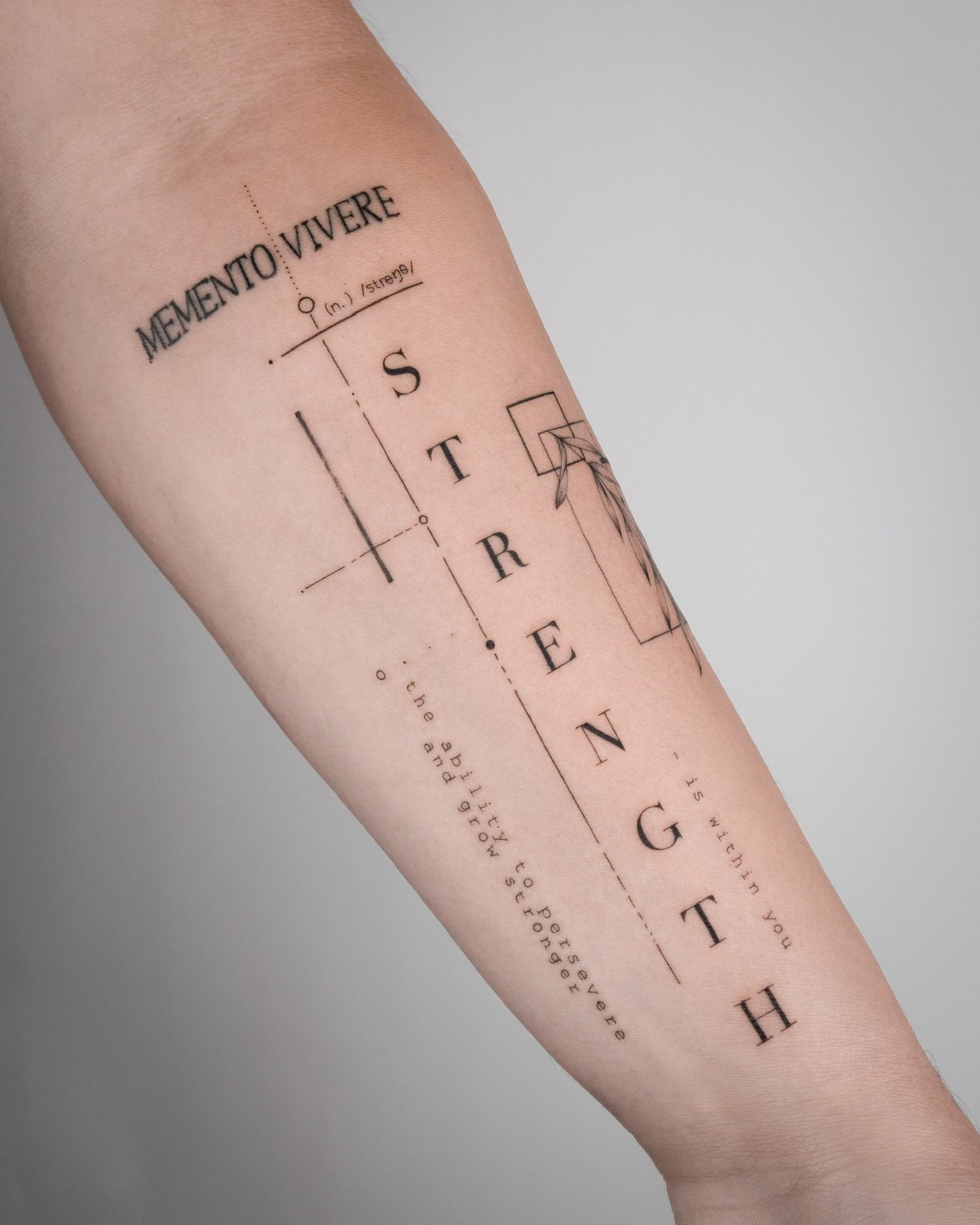 Tattoo on arm with the word 'MEMENTO VIVERE' and various structural lines, geometric shapes, and additional text.