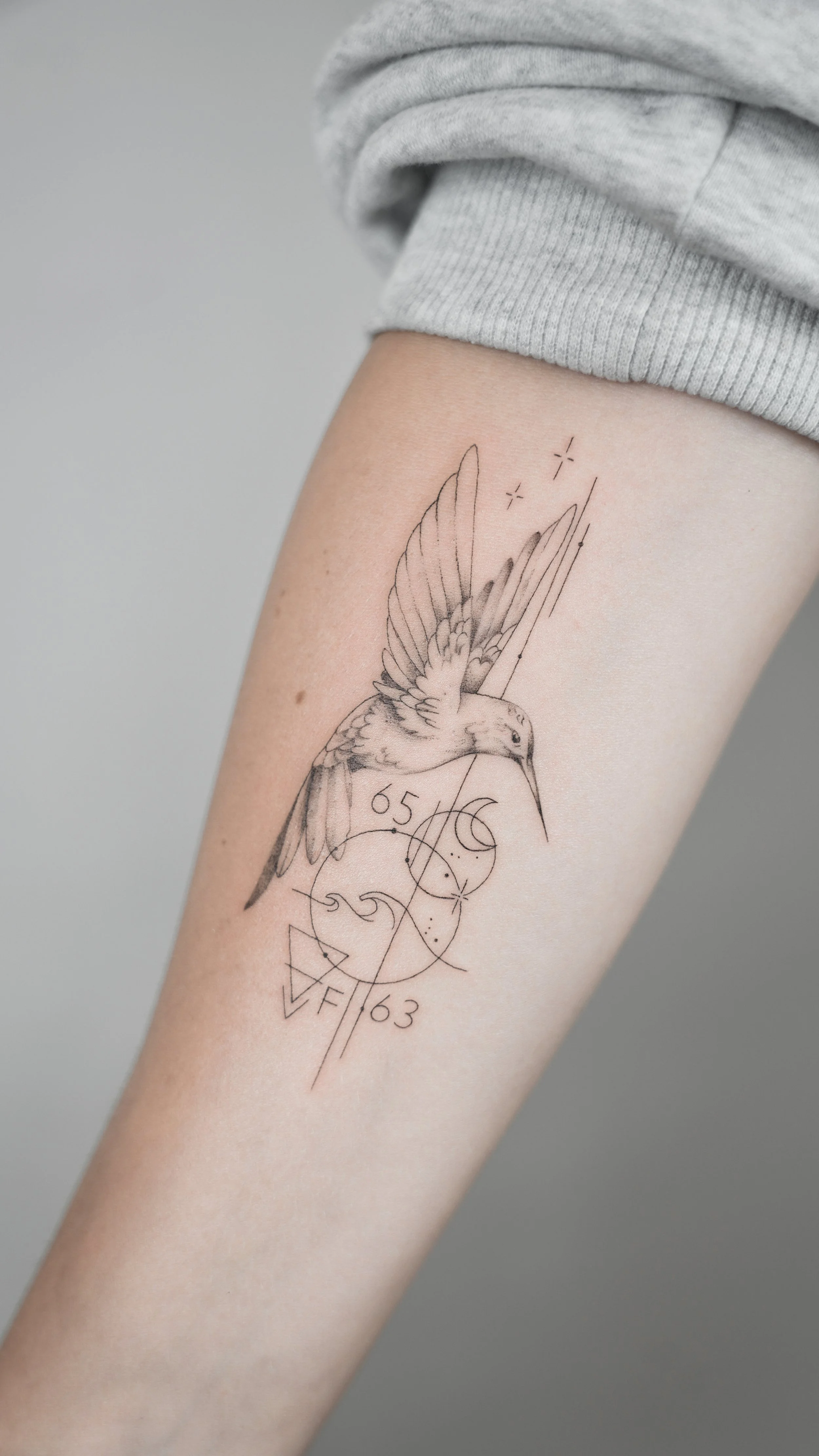 Tattoo of a hummingbird with geometric shapes and lines on person's thigh.