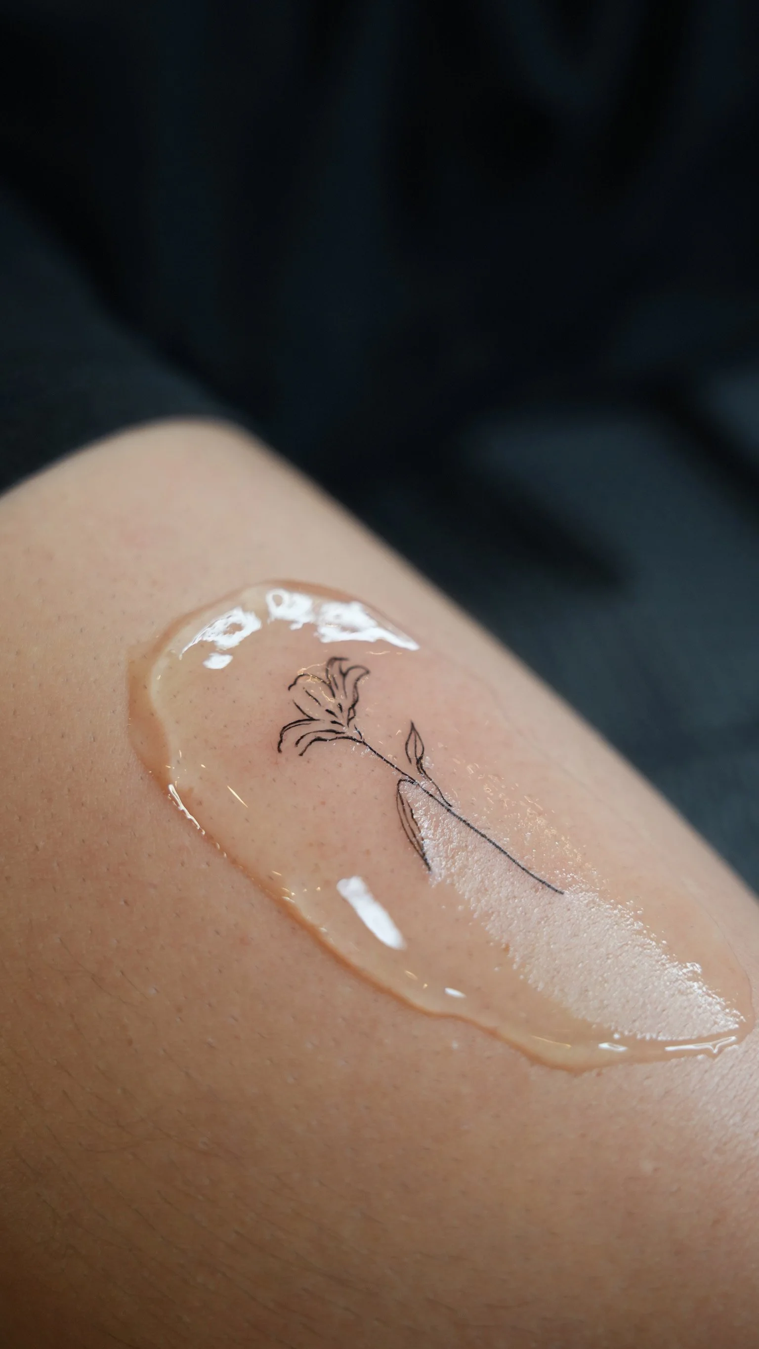 A close-up of a person's skin with a decorative illustration of a flower drawn with a thin black line inside a heart-shaped gel or liquid patch.