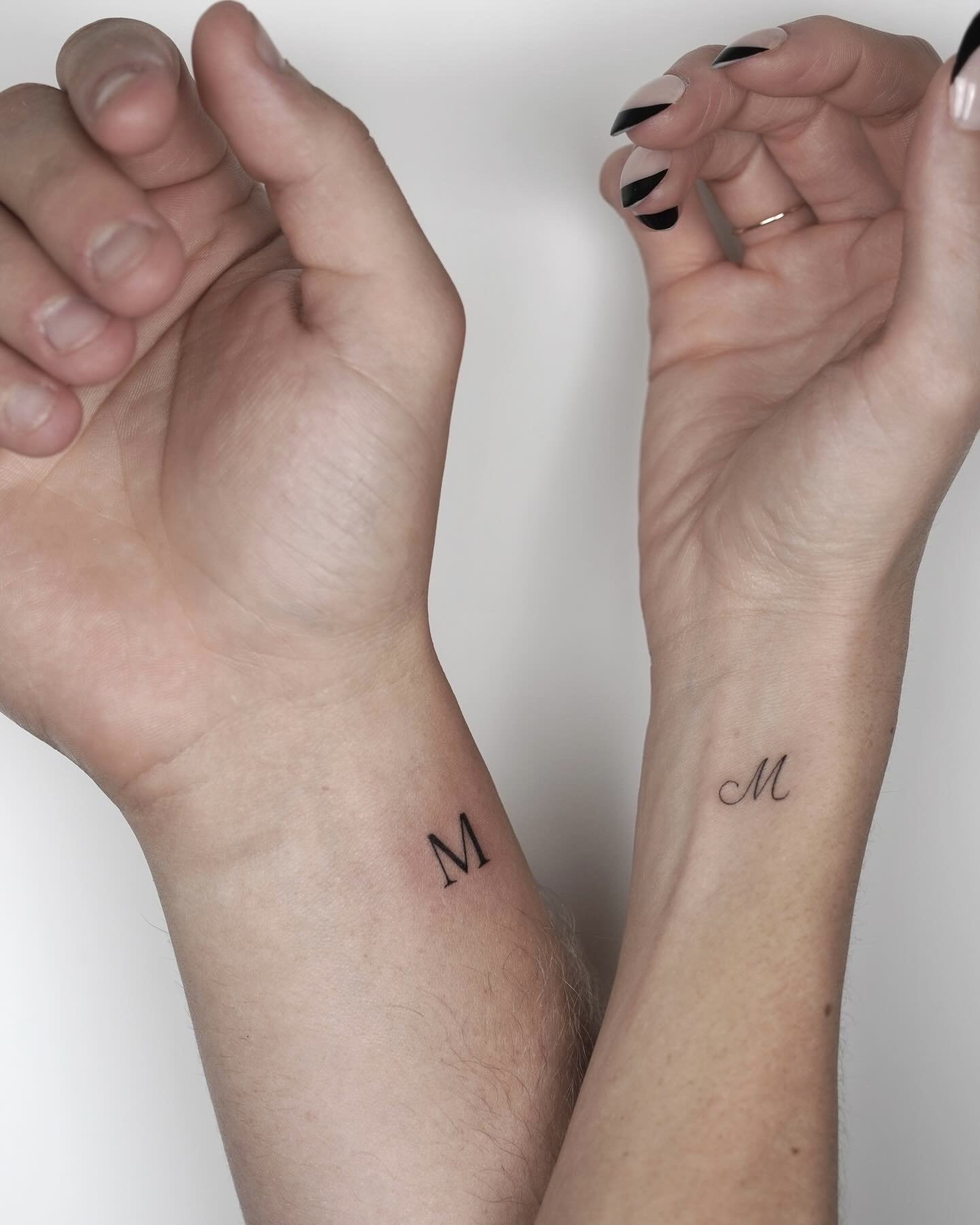 Close-up of two hands showing matching wrist tattoos with the letter 'M' on each wrist.