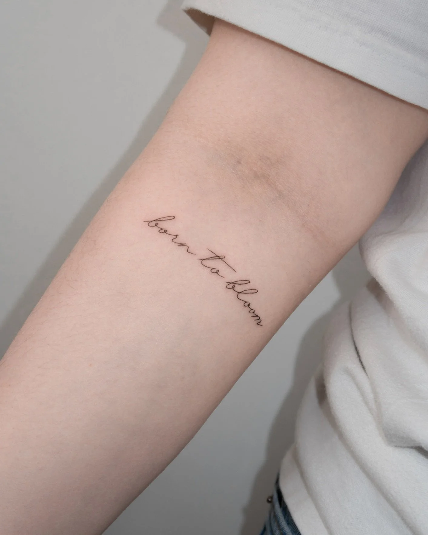 Tattoo on inner forearm with the words 'born to blossom' in cursive script.