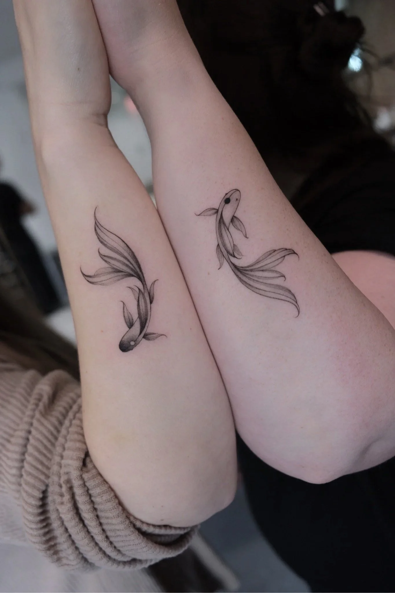 Close-up of a person's arm with a tattoo of a koi fish surrounded by flowing water.
