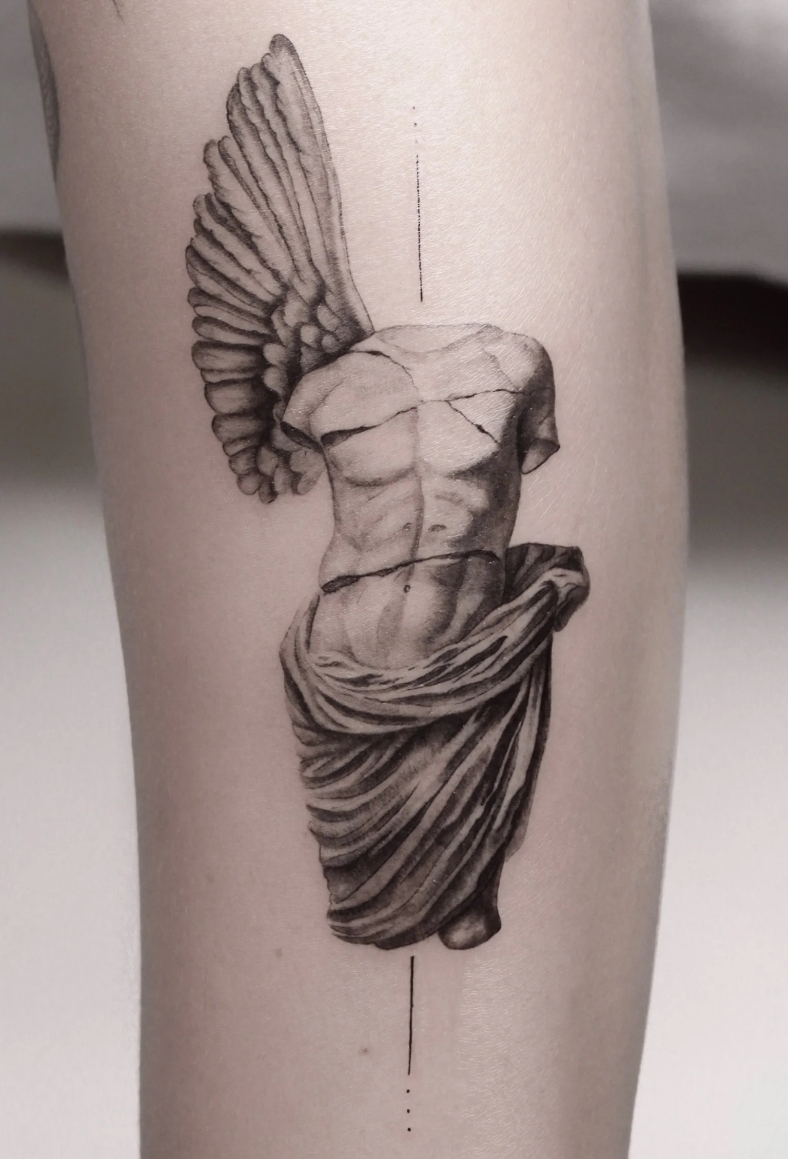 Tattoo of a cracked classical sculpture torso with one wing, wrapped in cloth, on person's arm.