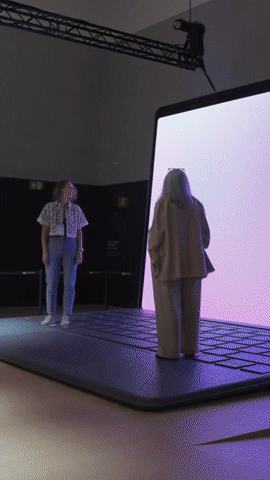 Two women standing in front of a large screen on an elevated stage in a dark room with a metal truss overhead.