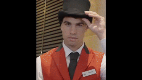 A young man wearing a black top hat, white shirt, black tie, and an orange vest.