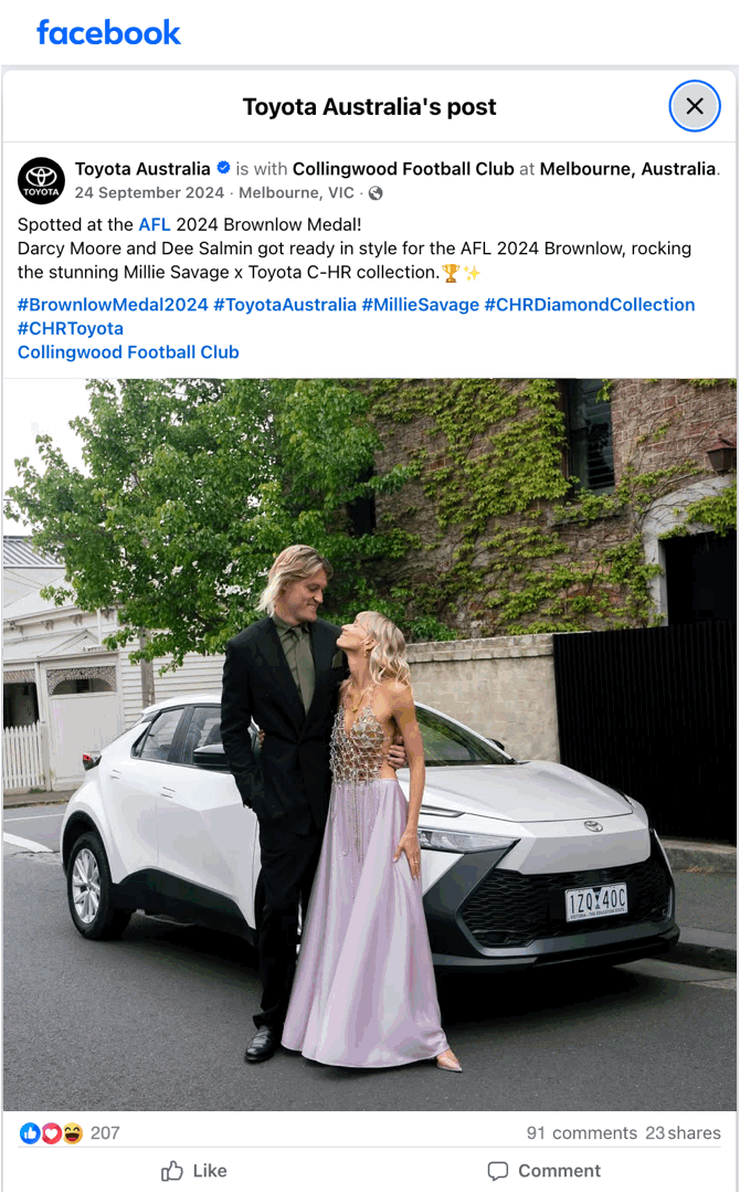 A man in a black suit and a woman in a long, elegant purple gown are standing close together in front of a white Toyota car, with a brick building and greenery in the background.