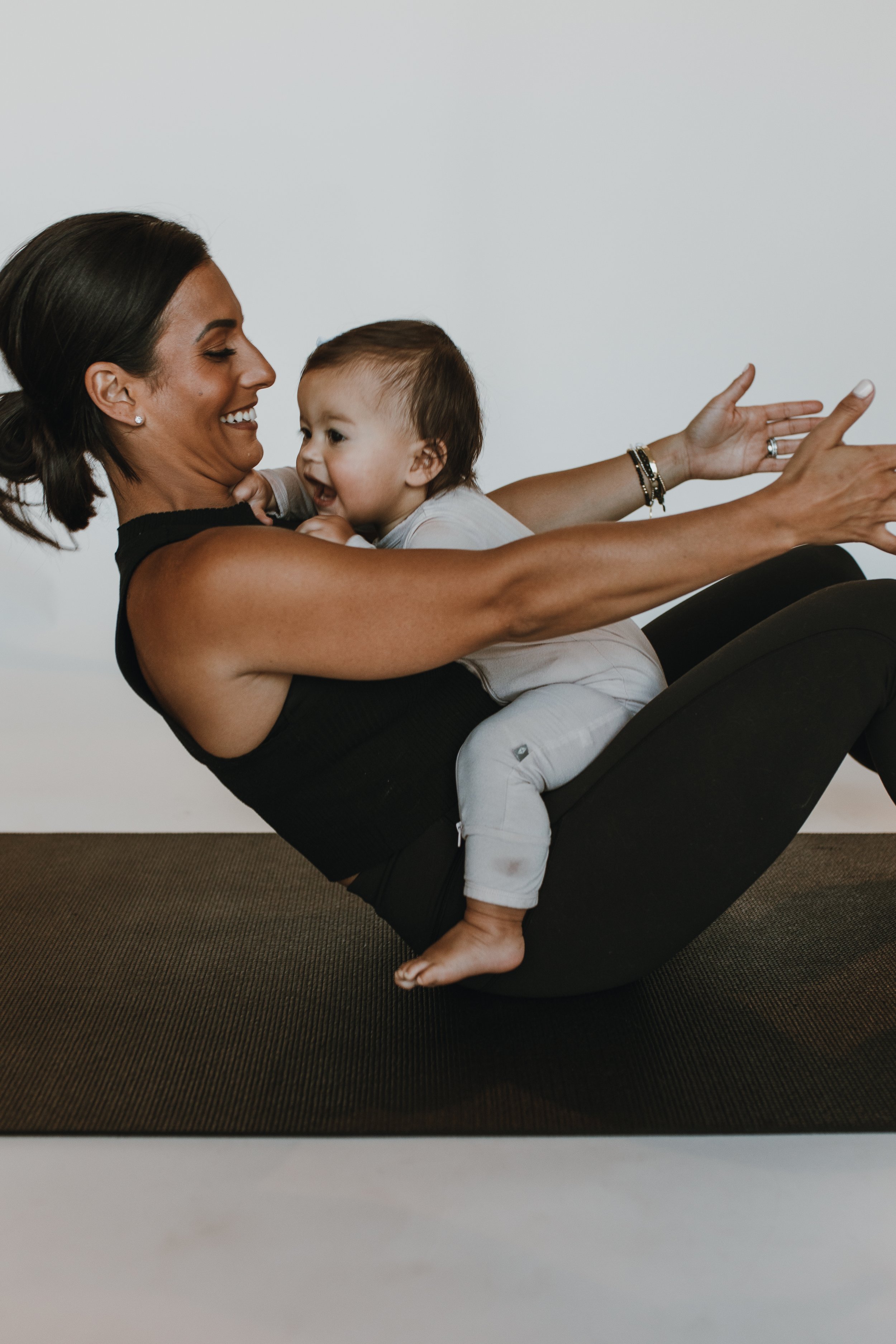 C_Wickson Studios Owner & Founder Cally Weymouth in boat yoga pose with baby sitting in lap