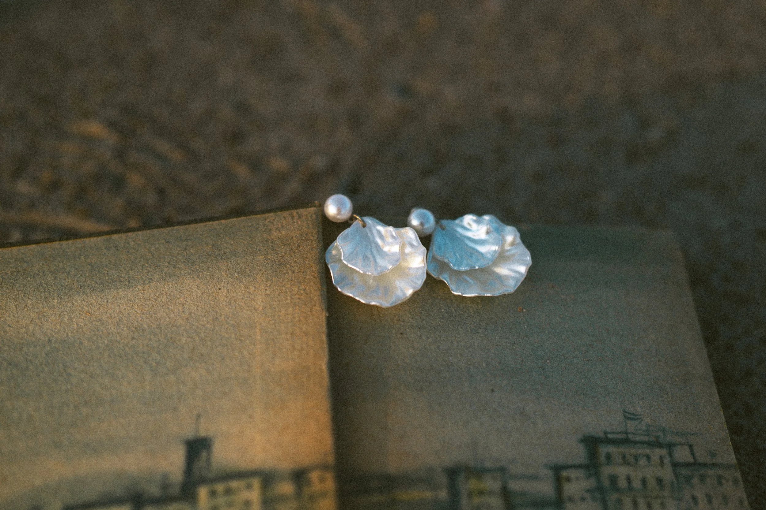 A pair of silver earrings with pearl-like beads resting on a darker surface.