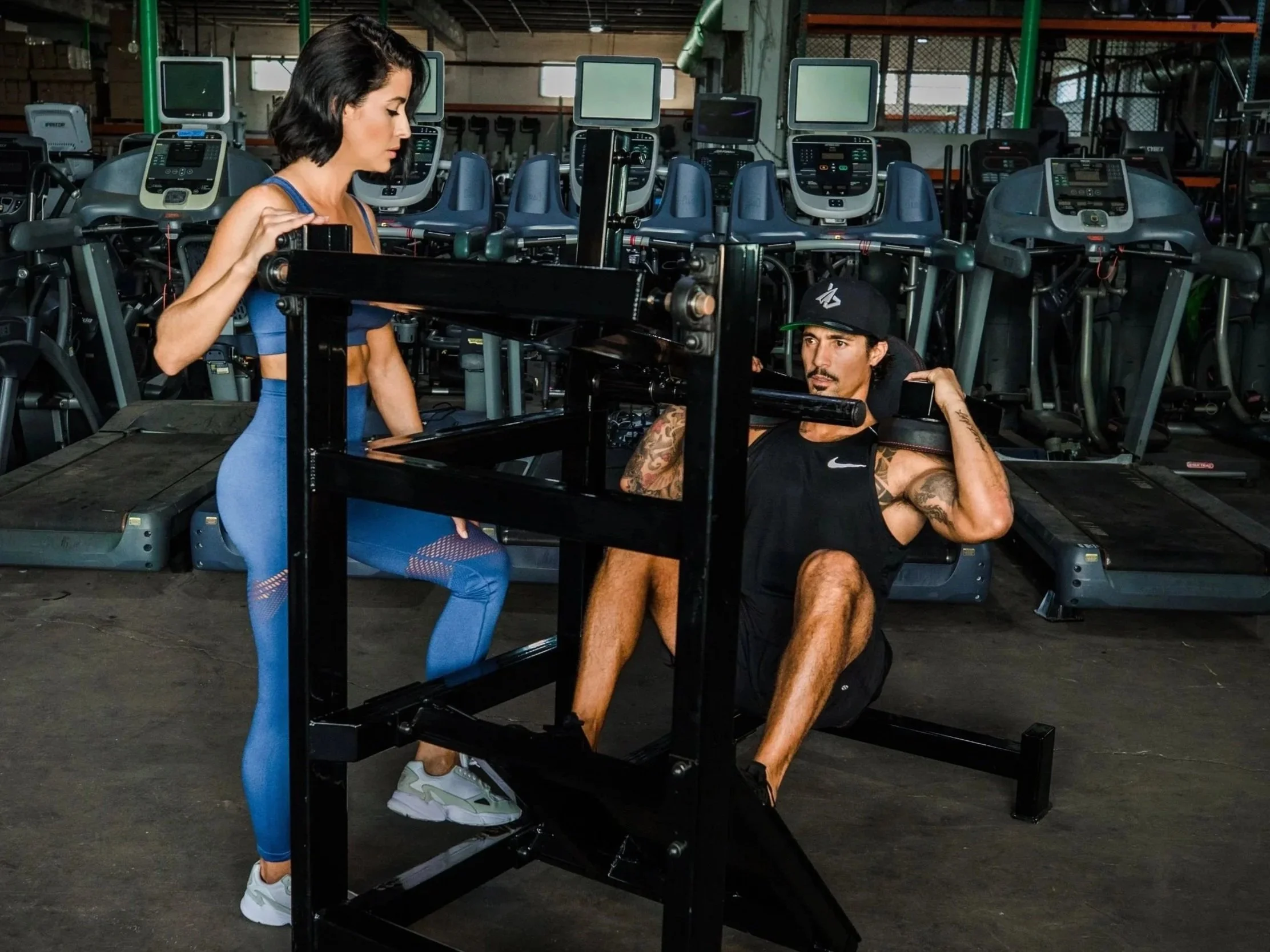 Personal training session coaching proper form on squat machine at gym