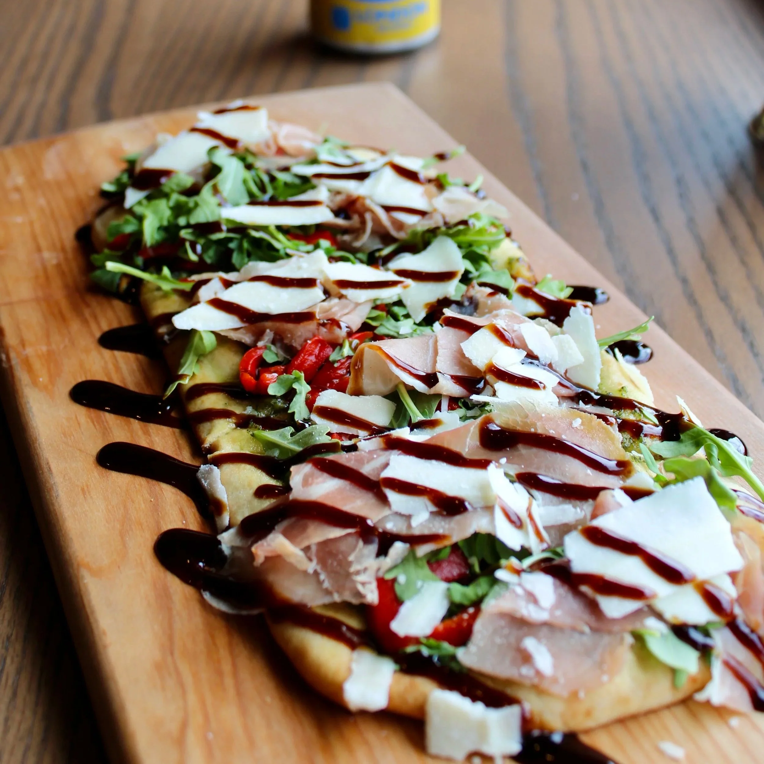Mediterranean Flatbread
Crispy flatbread topped with vibrant basil pesto, peppery arugula, sweet cherry tomatoes, prosciutto, and balsamic glaze. Finished with shaved Parmigiano.
