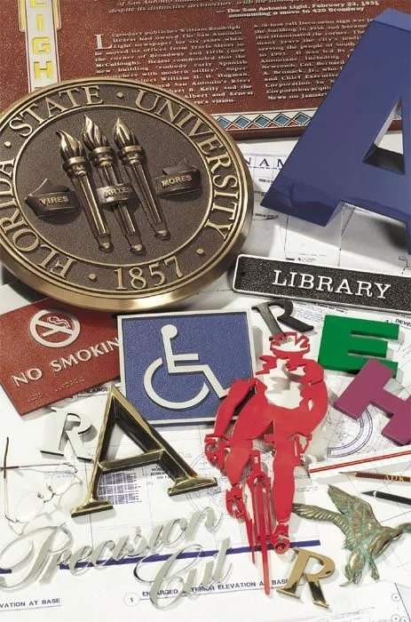 Collection of ADA signage components including tactile letters, Braille, accessibility symbols, and safety icons used in compliant architectural signage by A.R.K. Ramos.