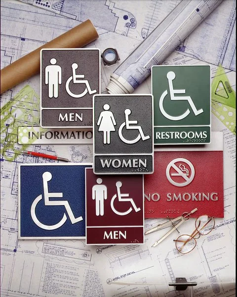Assortment of ADA-compliant signs featuring raised lettering, Braille, and contrasting color backgrounds in metal finishes