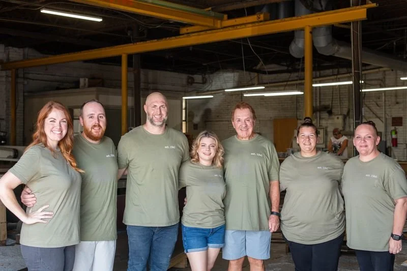 A team of A.R.K. Ramos employees standing together inside their foundry, showcasing the craftsmanship behind their precision-cast memorial plaques. The group reflects the company's commitment to high-quality, durable signage and memorials.