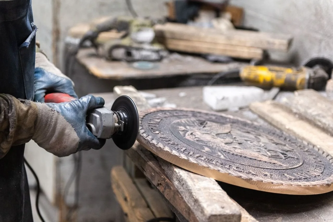 Sign restoration process showing a craftsman refinishing metal by grinding and smoothing the edge of a cast plaque, restoring detail, durability, and finish at A.R.K. Ramos.