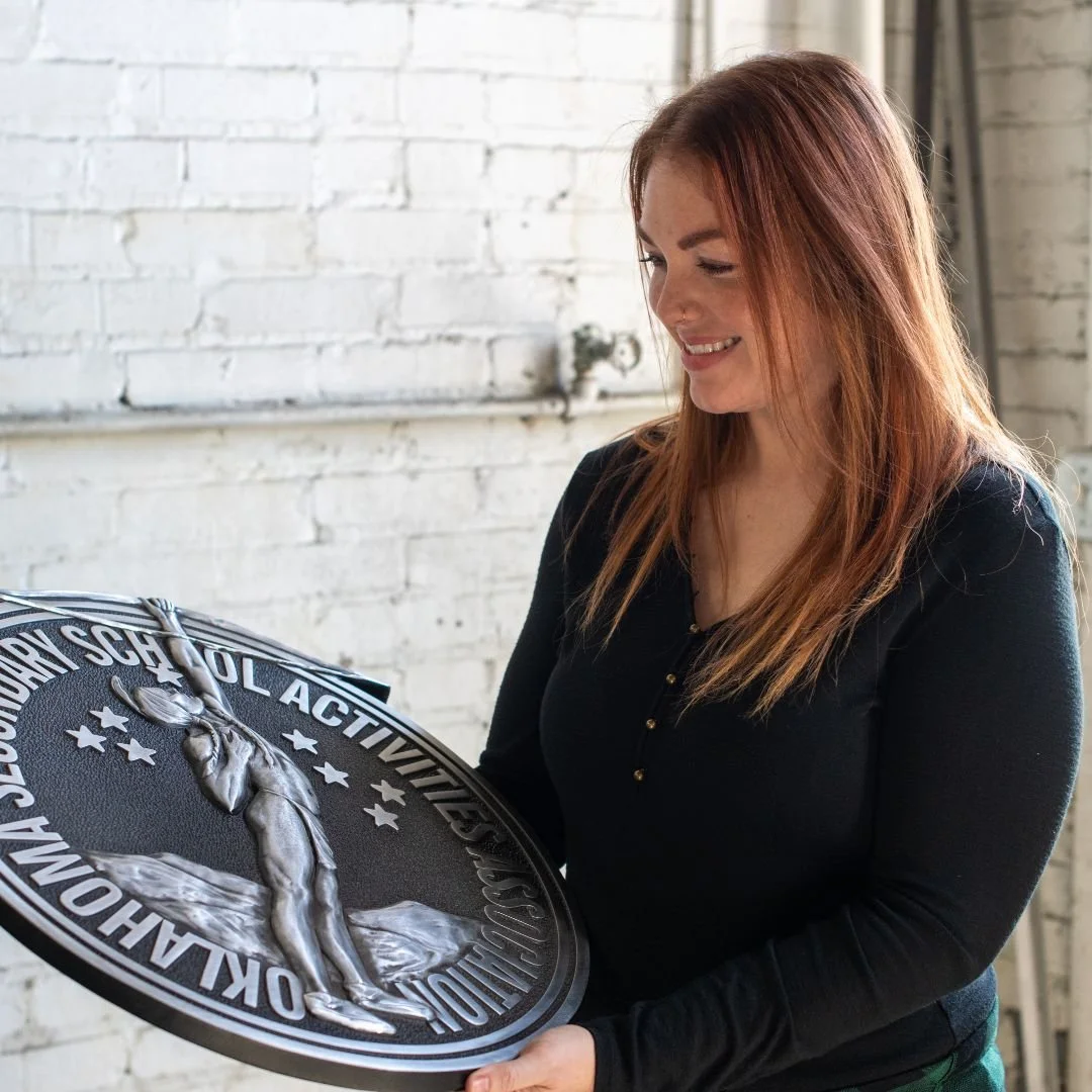 A.R.K. Ramos team member holding custom cast architectural signage manufactured for Division 10 commercial projects.