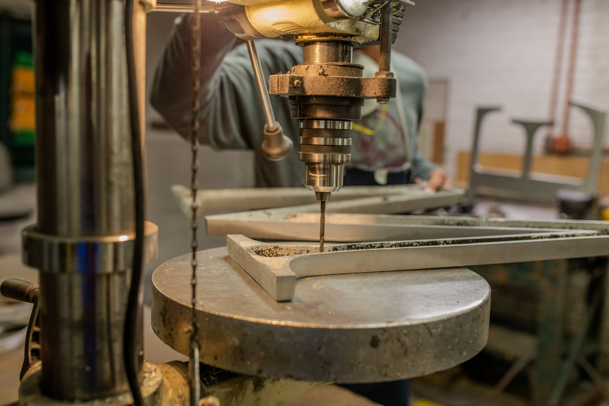 A.R.K. Ramos craftsman precision-drilling custom metal lettering, showcasing foundry services for architects and Division 10 specialists specifying architectural signage.