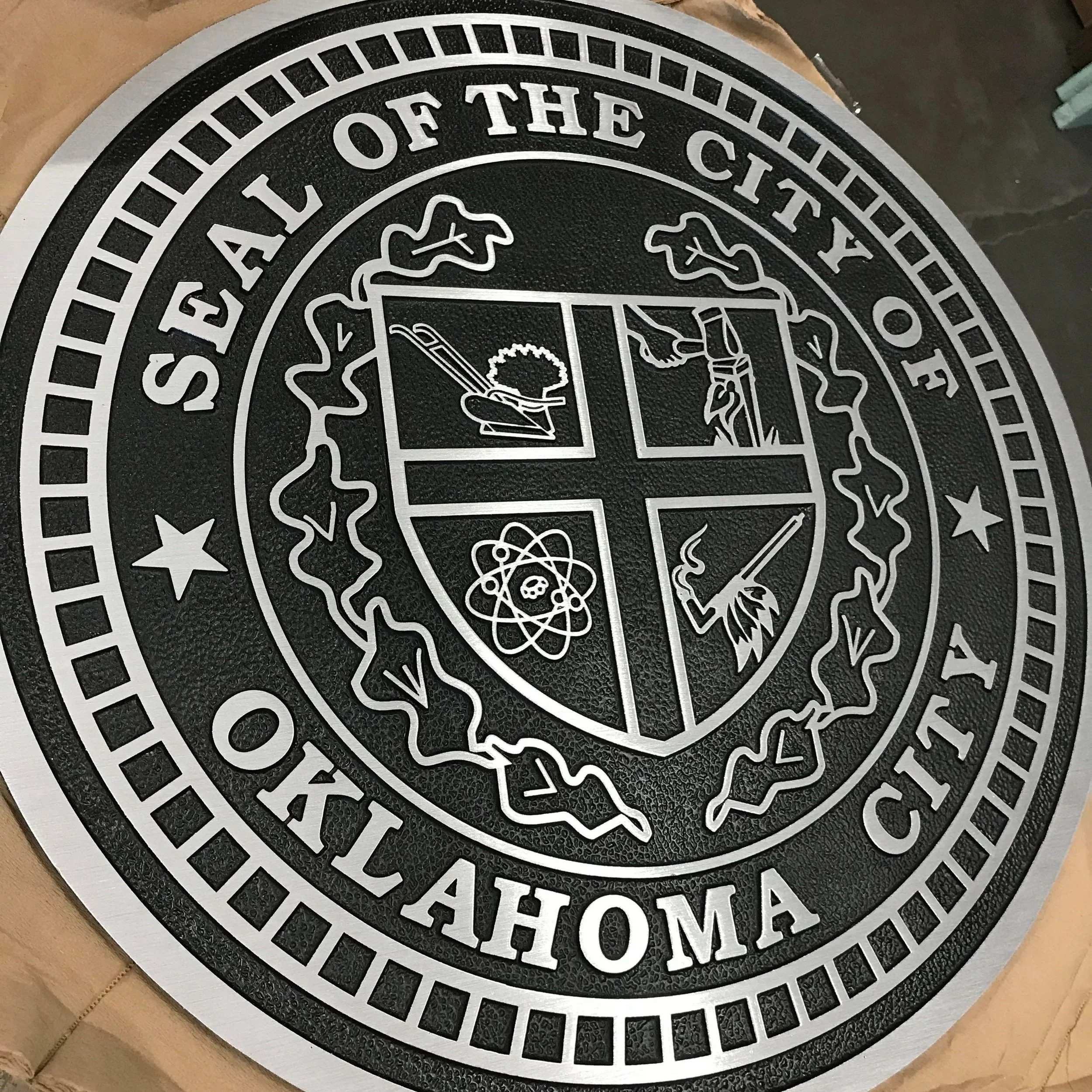 Custom City of Oklahoma City metal seal with raised silver lettering and detailed crest on a textured black background, demonstrating precision foundry services for Division 10 specifying.