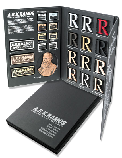 Display of the A.R.K. Ramos sample kit including cast plaques, metal letters, etched pieces, and various finish options arranged in a presentation box
