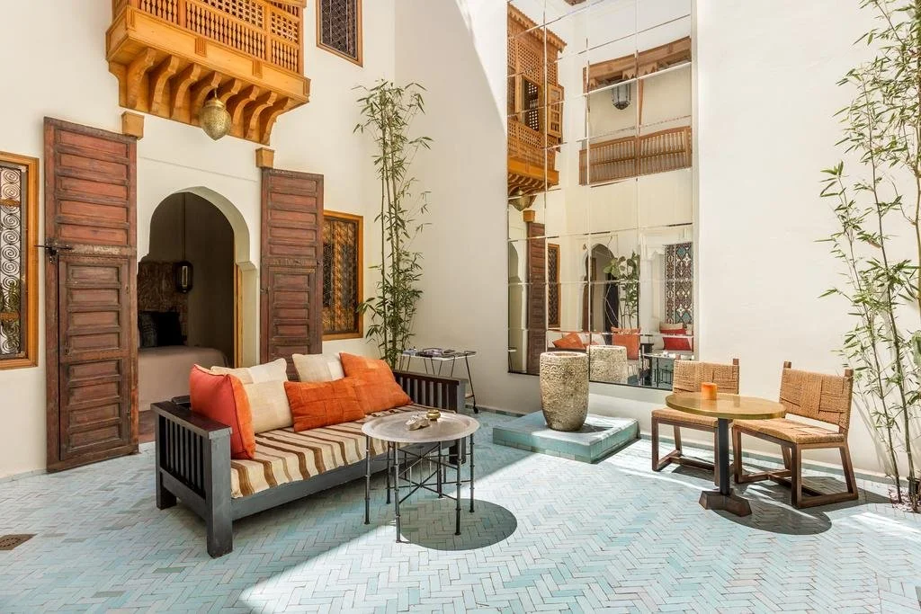 Indoor outdoor patio with white walls, wooden doors, plants, and seating areas including a sofa with cushions and a small table, and chairs with a candle.
