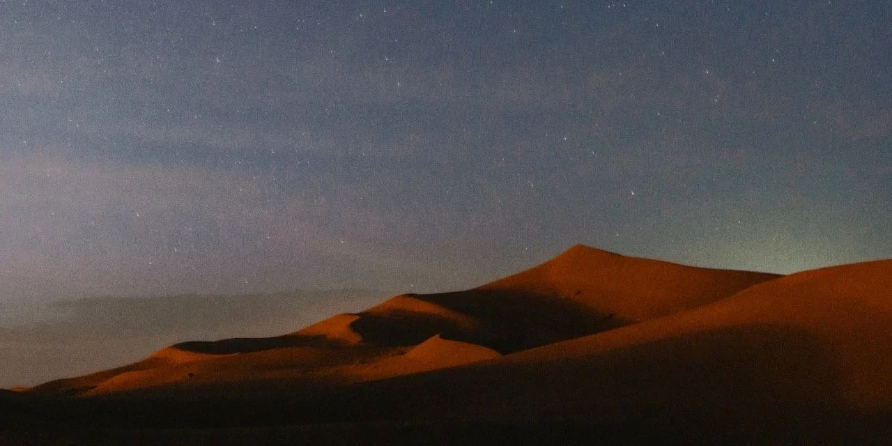Nighttime desert scene with sand dunes and a starry sky.