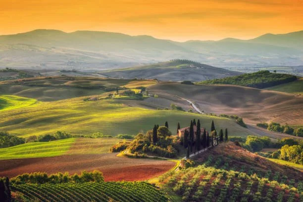 Rolling hills and farmland at sunset in the Tuscany region of Italy.