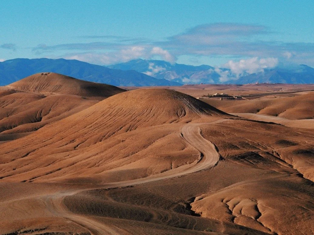 Rolling desert hills with dry, winding dirt roads and distant mountain range under blue sky