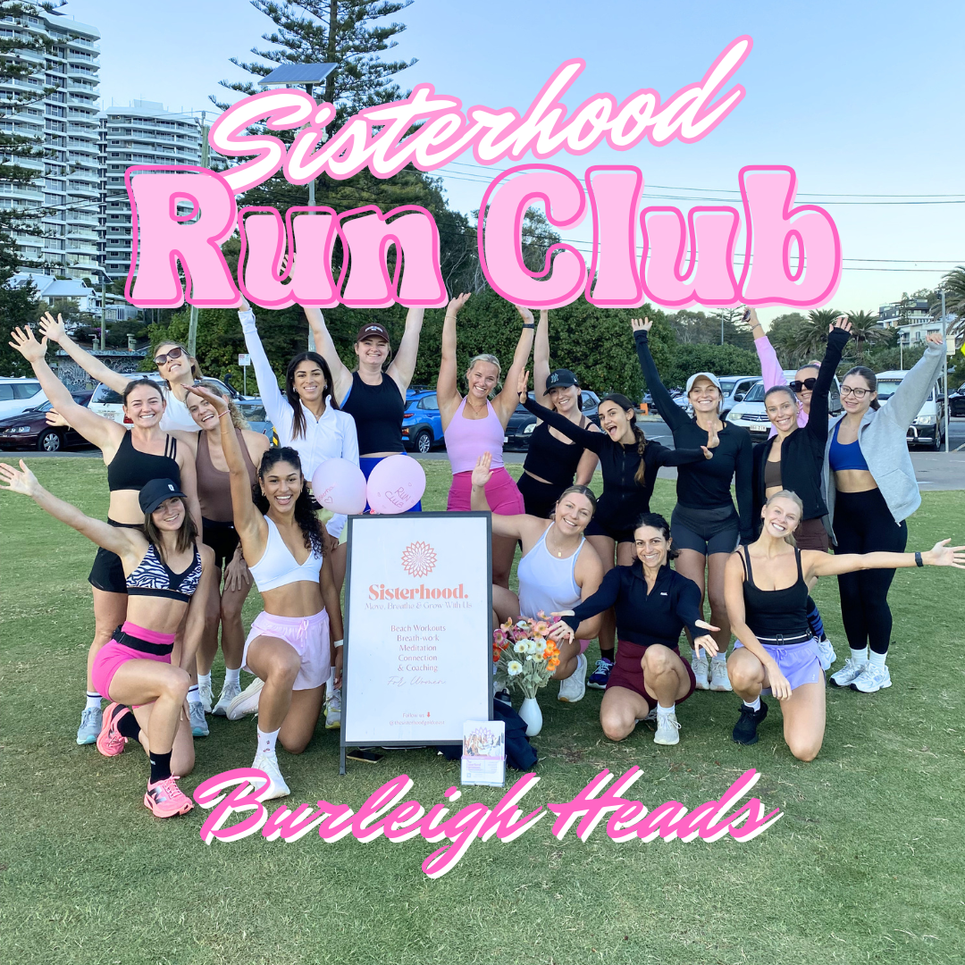 A group of women walking on the beach near the ocean, participating in a sisterhood run club event, with a city skyline in the background.