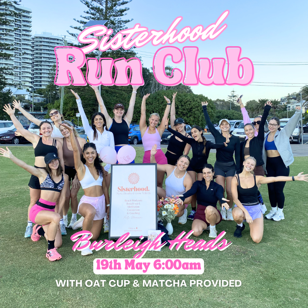 A group of women walking on the beach near the ocean, participating in a sisterhood run club event, with a city skyline in the background.