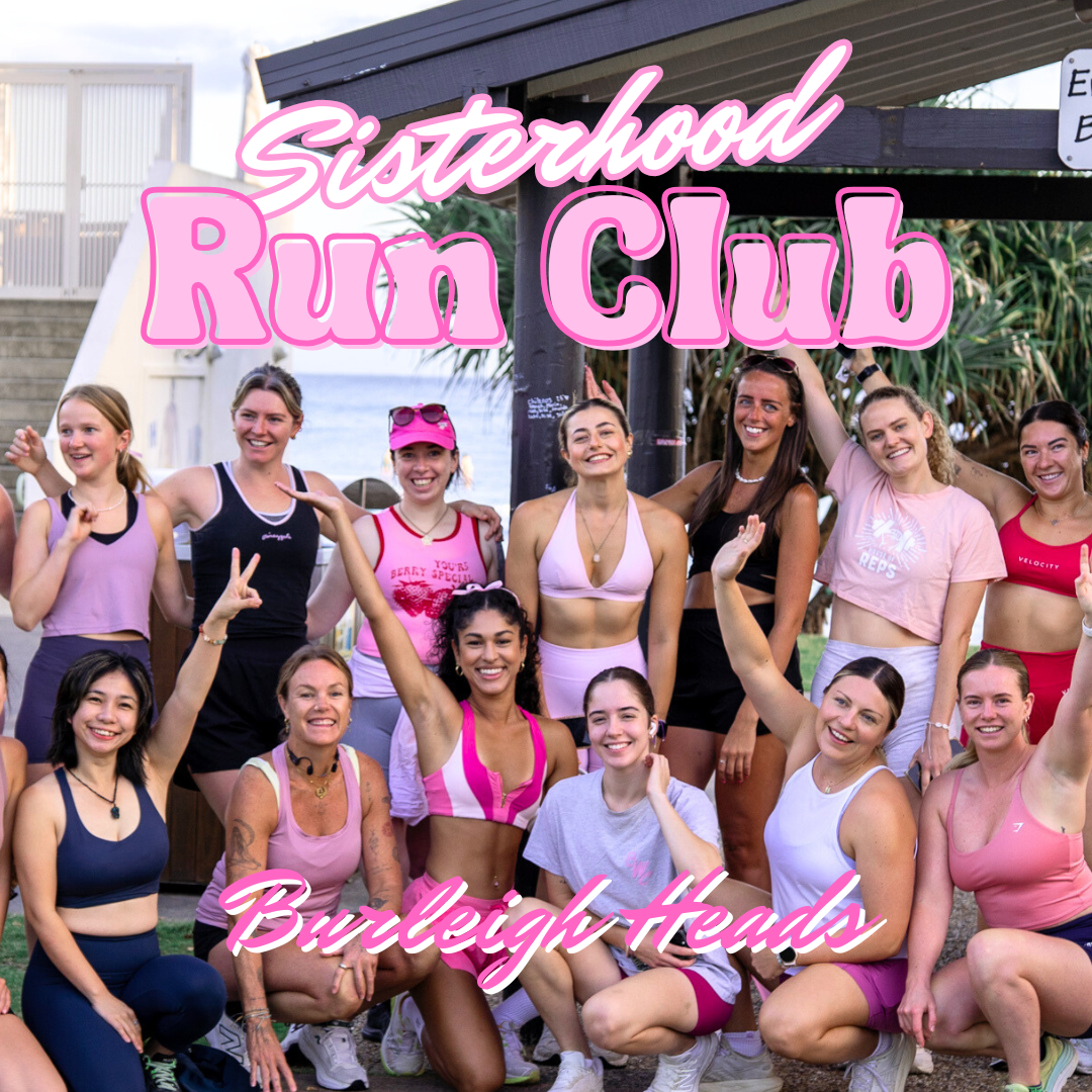 A group of women walking on the beach near the ocean, participating in a sisterhood run club event, with a city skyline in the background.