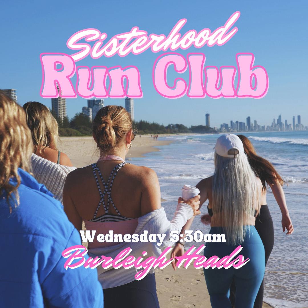 A group of women walking on the beach near the ocean, participating in a sisterhood run club event, with a city skyline in the background.