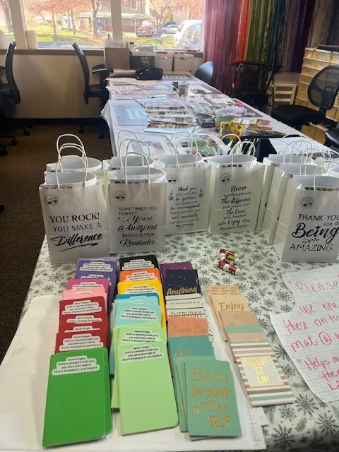 Table covered with gift bags, motivational cards, and small wrapped candies in a room with windows and chairs.