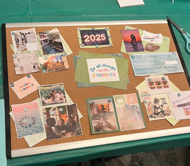 A corkboard with various photos, notes, and decorative items pinned to it, including the words 'Do all things with kindness' and the year '2025'.