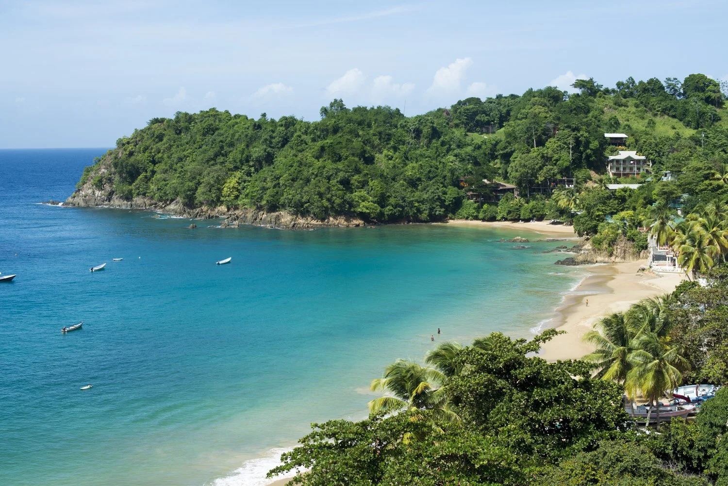 Castara Bay in Tobago, with a golden sandy beach, clear turquoise Caribbean Sea, fishing boats and rainforest covered hills