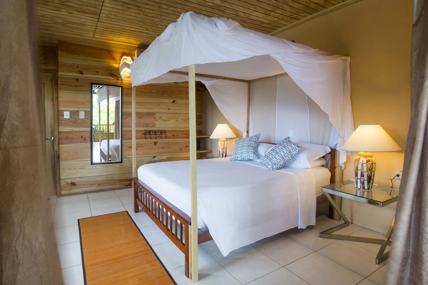 Bedroom in an eco lodge at Castara Retreats, Tobago, with a four poster bed, white mosquito net and wooden walls