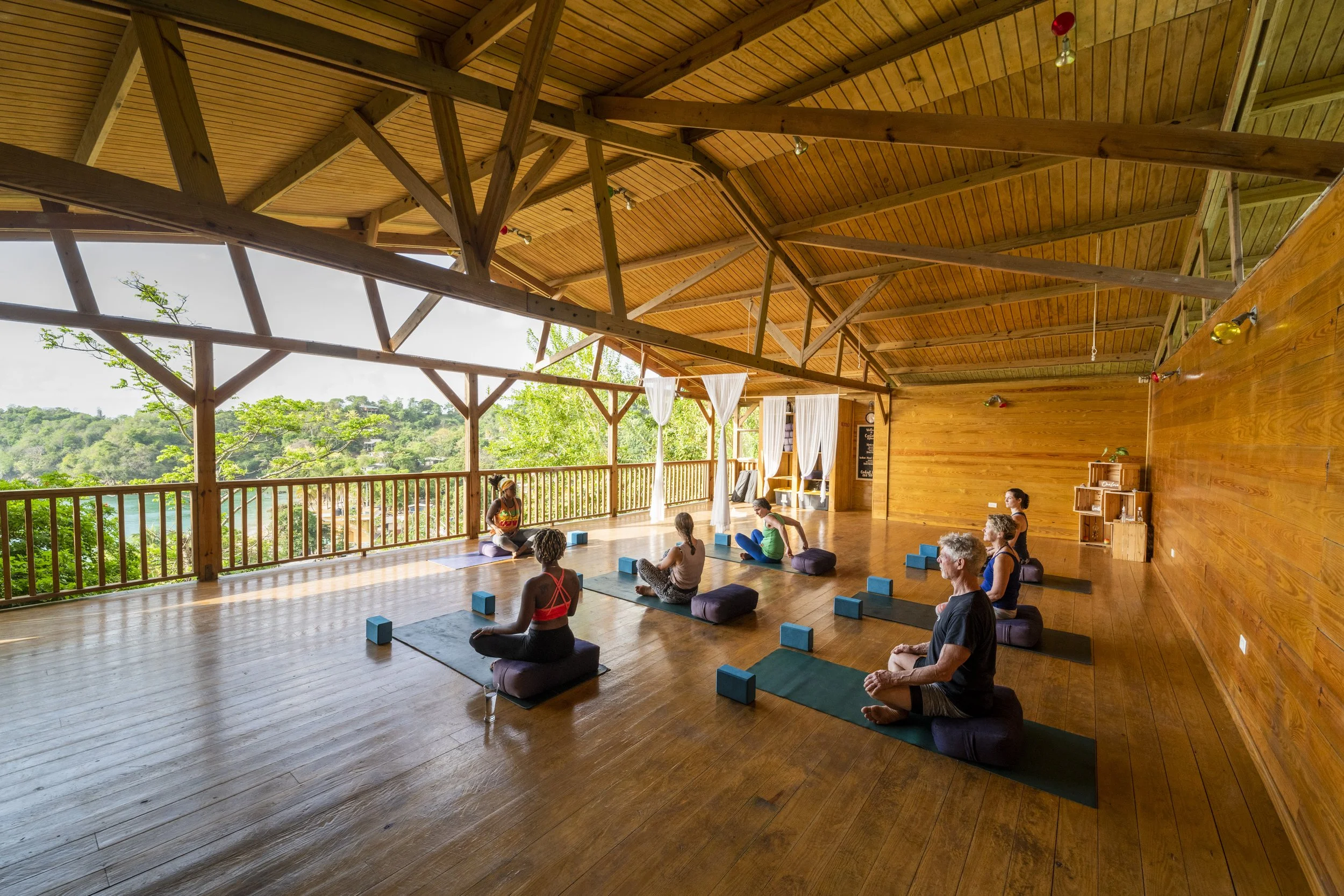 Group yoga and breathwork class in the open air wooden yoga studio at Castara Retreats, overlooking the rainforest and Castara Bay, Tobago