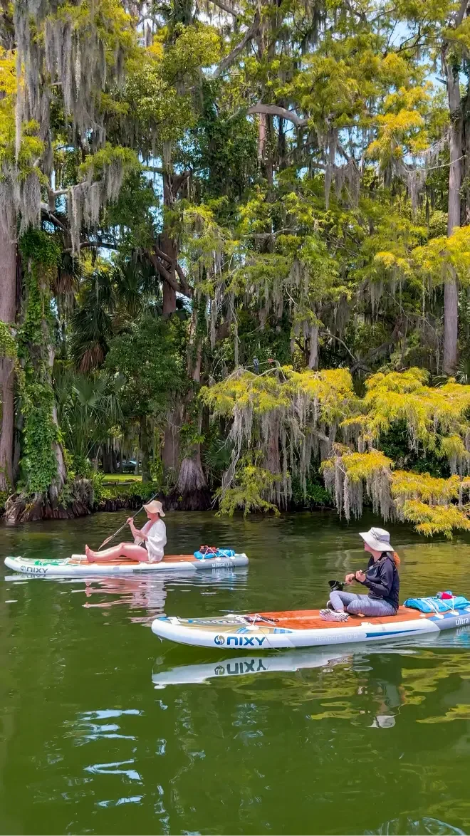Two people paddleboarding on calm waters on the Winter Park Chain of Lakes with Otter Paddle Orlando.