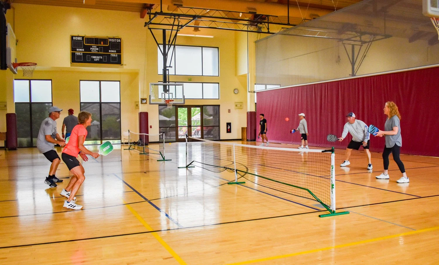 Two groups of 4 playing pickleball set up in the indoor gym 