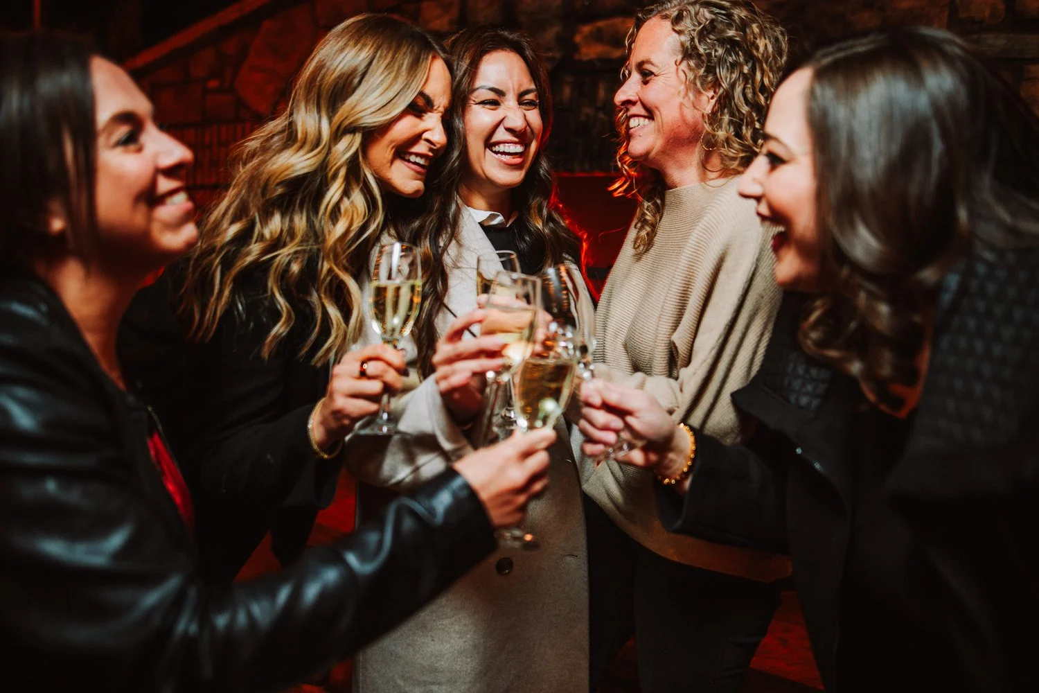 Group of women celebrating with champagne glasses in a cozy fireplace setting.
